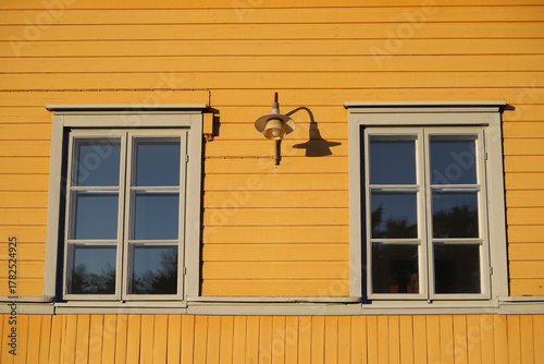 Facade of a yellow-painted house in classic Scandinavian style, featuring two windows and an exterior wall lamp, Porvoo, Finland
