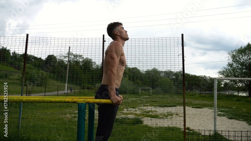Vászonkép Young sportsman doing push ups on parallel bars at nature