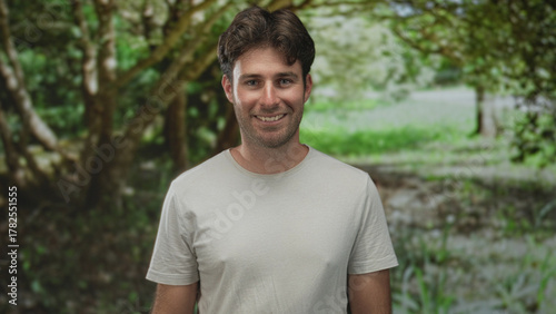 Man smiling with face visible and relaxed posture in a green park forest setting; serenity friendly.