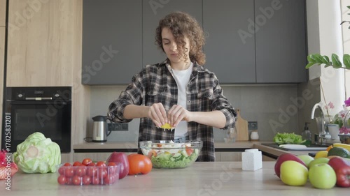 Woman Squeezing Lemon Juice On Fresh Vegetable Salad In Modern Kitchen