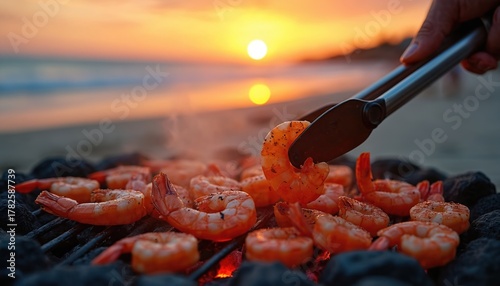 Fototapeta Naklejka Na Ścianę i Meble -  Shrimp grilling on charcoal barbecue grill at beach at sunset. Hand with tongs holds prawn. Delicious grilled seafood cooking outdoors. Summer tropic holidays, vacation, travel mood. Tasty dinner.