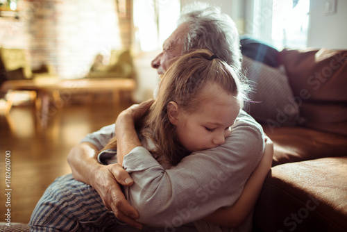Senior grandfather and child granddaughter share a comforting hug at home