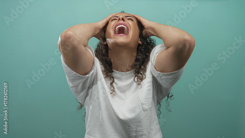 Foto Young hispanic woman screaming with mouth wide open in a mint green studio setting; frustration