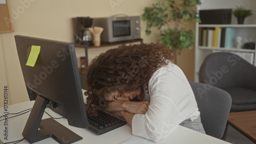 Hispanic woman resting head on computer keyboard at work desk in office late after long shift; fatigue.