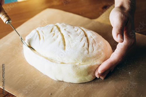 Foto Hand scoring artisan sourdough bread dough on wooden surface