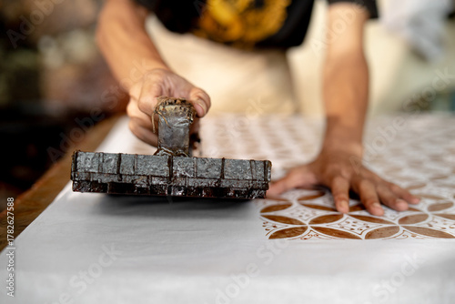 close up of batik maker pressing copper stamp ( BATIK CAP ) dipped in hot wax onto fabric, capturing manual craftsmanship and traditional textile printing in Pekalongan, Indonesia.