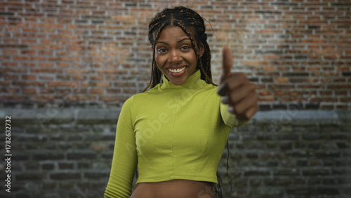 African american woman in green cropped top smiling then frowning while giving thumbs up then thumbs down in building; confidence decision.