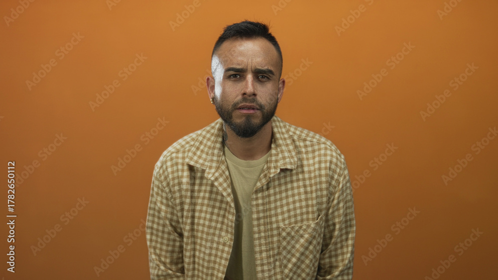 Obraz premium Man frowning with visible face and beard, leaning slightly forward in an orange studio; introspection.