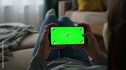 Green Screen girl using smartphone with in living room watching movie video content young woman at home lying on couch tracking markers smart phone a horizontal position indoors closeup scene 1
