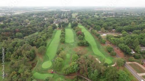 Drone aerial of cloudy green landscape of a midwest American golf course country club in Ohio, with golfers, carts, courses, holes, and trails along residential landscape near buildings and forest