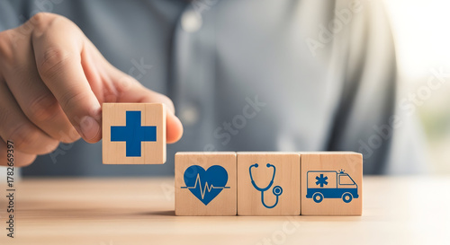 Hand holding wooden block with health insurance icon with heart, stethoscope, ambulance
