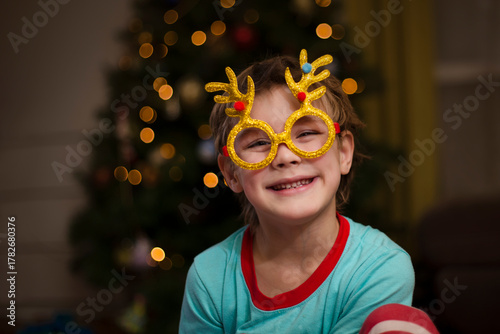 kid boy  Wearing carnival glasses with Christmas decor on near the Christmas tree at home. 