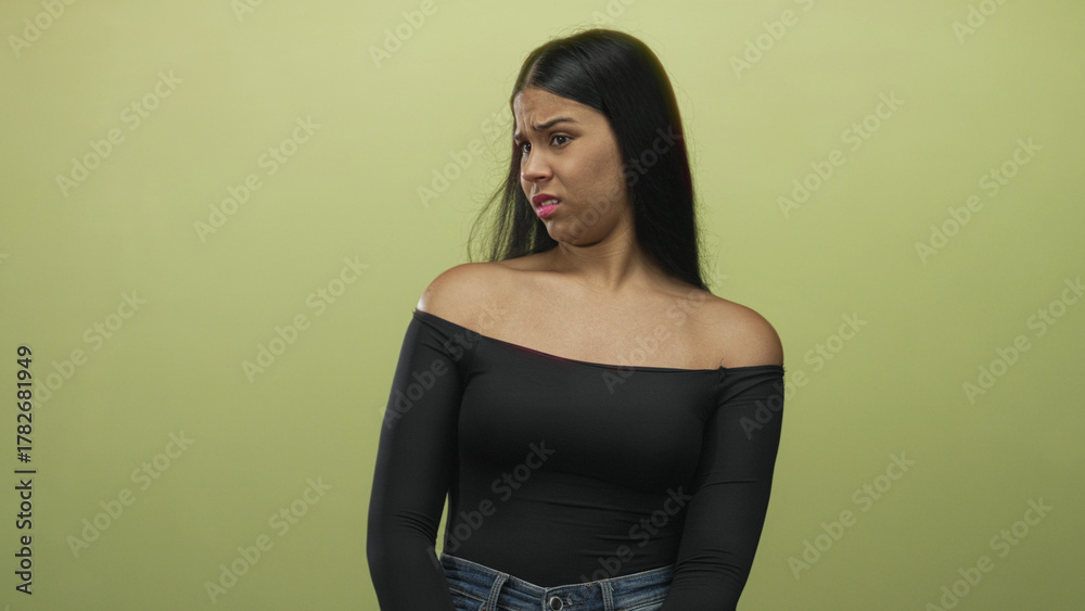 Naklejka premium Woman glances to side showing bare shoulder against green wall in studio under soft lighting; disgust.