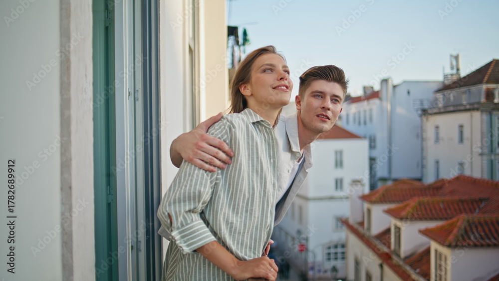 Obraz premium Young couple admiring cityscape from balcony. Affectionate husband embracing