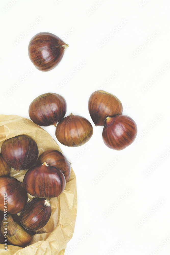 Obraz premium Chestnuts on a white background and paper bag, zenith view. In vertical.