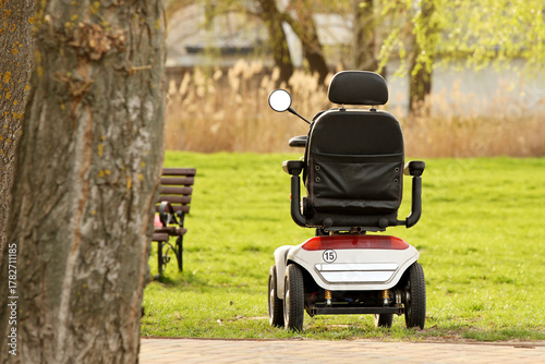 An electric wheelchair stands in a summer park near a tree. Automation and mechanization of assistance to disabled and elderly people with problems moving their own legs. Caring for those in need
