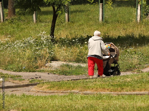 An elderly woman walks with a pram among the summer greenery. A governess is nursing a child on the street. Raising children zorovym and seasoned. Baby sleep in the fresh air. Socialization of older