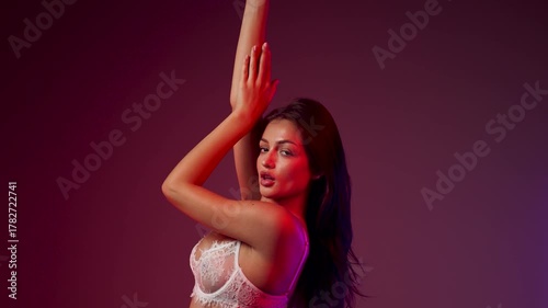 Woman poses in white lingerie under colorful neon lights in a studio setting
