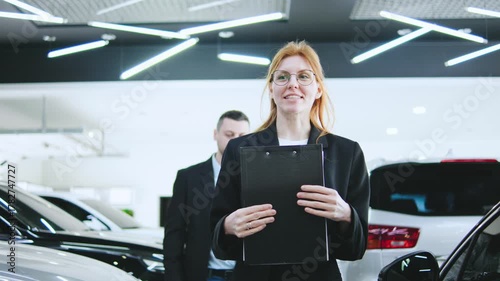 Saleswoman guides clients happy couple through a car dealership for consultation and test drive preparation, ensuring a smooth buying experience
