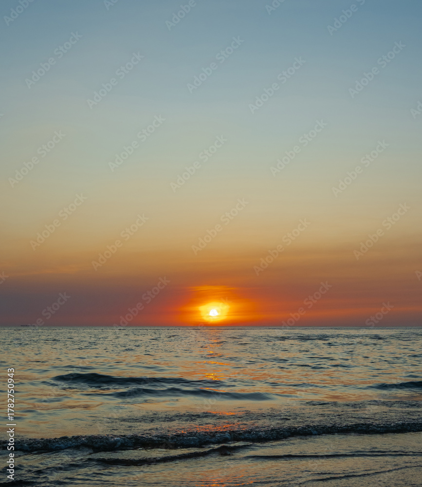 Fototapeta premium serene vertical image capture beauty sunset over calm ocean. sun low on horizon casting warm golden glow across sky and reflect off gentle wave. warm orange near creating peaceful calm atmosphere.