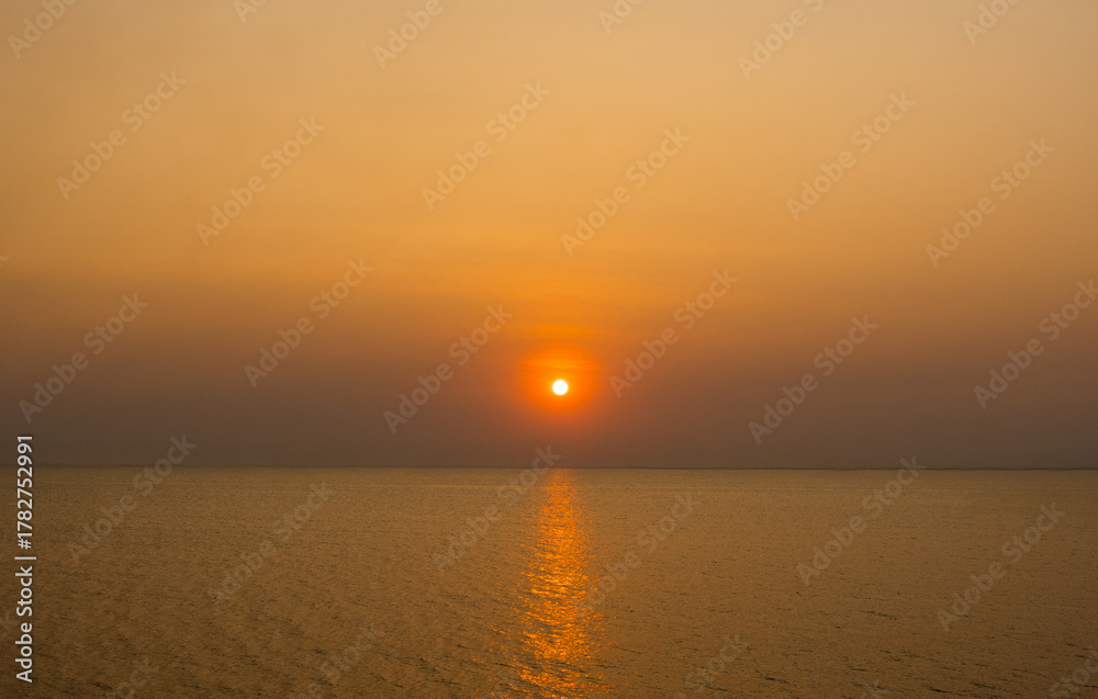 Fototapeta premium serene panorama image capture beauty sunset over calm ocean. sun low on horizon casting warm golden glow across sky and reflect off gentle wave. warm orange near creating peaceful calm atmosphere.