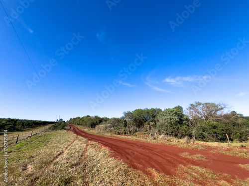 Red Dirt Road Through Countryside Under Clear Blue Sky