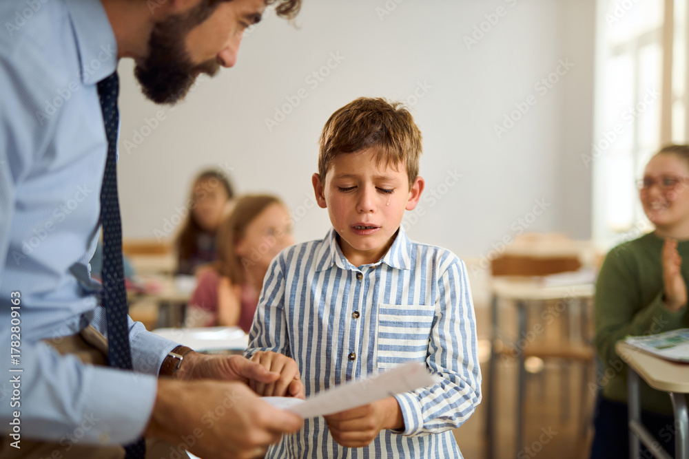 Fototapeta premium Elementary student crying while receiving test results on a class in the classroom, comforted by the teacher.