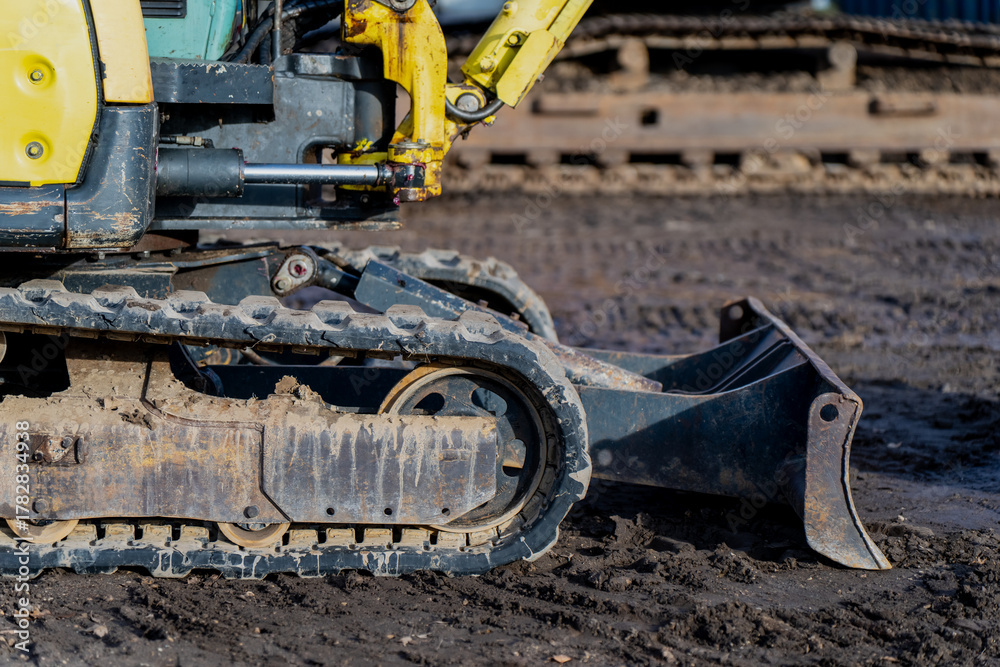 Fototapeta premium Tracked mini excavator on construction site showing rubber crawler system, hydraulic arm and metal bucket representing industrial machinery use, groundwork operation and excavation process