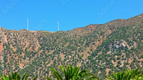 Mountain ridge with green bushes and wind turbines on background in clear blue sky on Kos Greece.