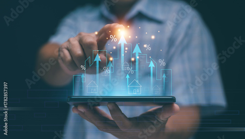 Real estate growth and financial technology concept. Hand holding smartphone with holographic buildings and upward arrows. Investment, property market, digital economy and percentage rate increase.
