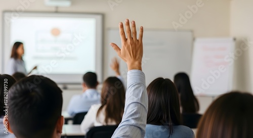 Active participation in an educational setting. A hand is up among a seated group of people, ready to contribute to the discussion.