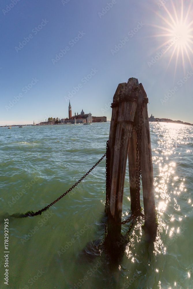 Fototapeta premium Wooden mooring post with chains in foreground and San Giorgio Maggiore island in background in Venice, Italy