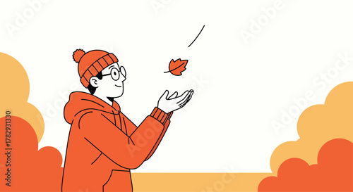 Young man in orange hoodie catches falling autumn leaf in park on crisp autumn day, enjoying the beauty of nature.