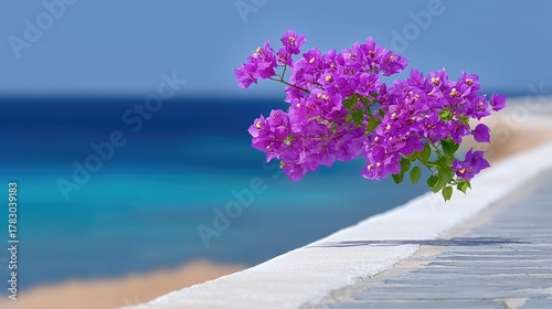Fototapeta Naklejka Na Ścianę i Meble -  Vibrant Pink Bougainvillea Flowers Bloom Against a Blurry Blue Ocean and Sandy Beach Under Bright Sunlight