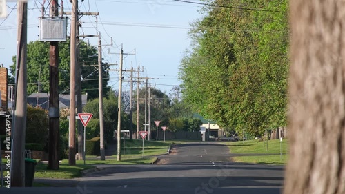 A quiet residential street in Camperdown, Victoria, Australia, with wooden power poles, overhead electrical lines, and a car passing through the leafy neighborhood. A regional Australian town