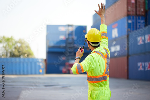 back view worker or engineer using walkie talkie and showing gesture to crane car in containers warehouse storage