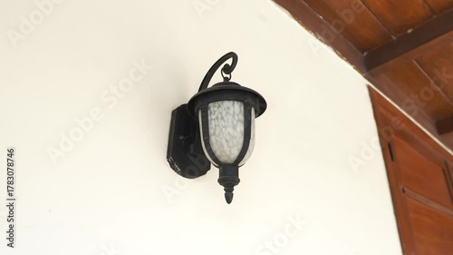 Close-up of a classic black vintage wall lamp with glass shade mounted on a cream wall, creating a warm and elegant exterior home atmosphere.