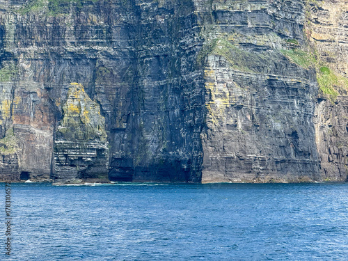Textured sea cliffs with colorful rock layers above deep blue ocean