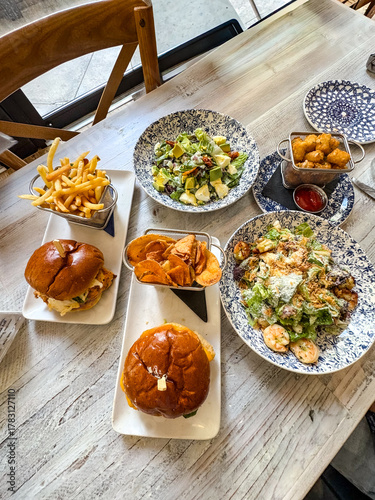 Assorted lunch spread with burgers, fries, salads and snacks on rustic table