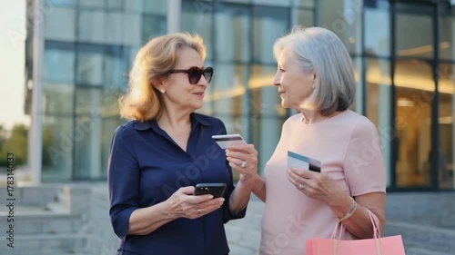 Shopping Spree with Friends: Two elegant women engage in a discussion during a shopping day, with credit cards in hand and surrounded by urban architecture.