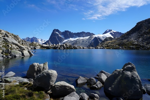 Mountain lake reflects the sky with snow capped peaks and rocky shorelines around it all