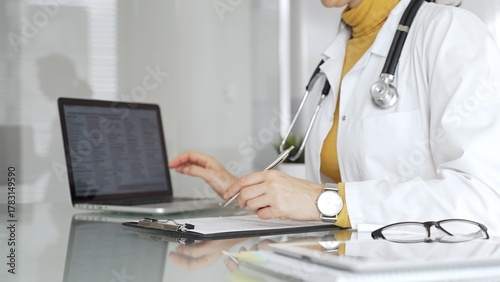Doctor working on medical records, writing prescription in clinic office, using laptop for patient data management. Medicine, healthcare and science concept