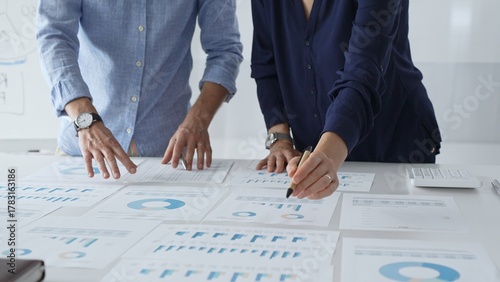 Professional team reviewing financial documents, pointing at charts on desk, collaborating to analyze data and strategize business growth. Business people concept