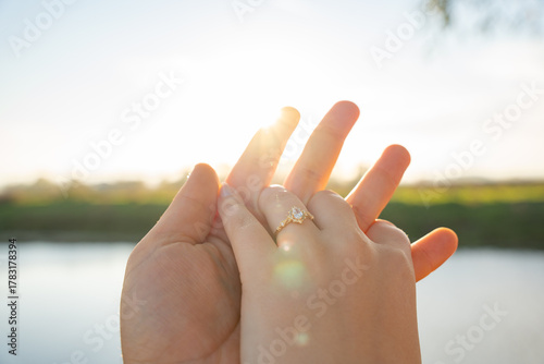 Ring on finger concept symbolizing love proposal marriage and romance in nature at sunset. Sunlit hand showing a gold engagement ring