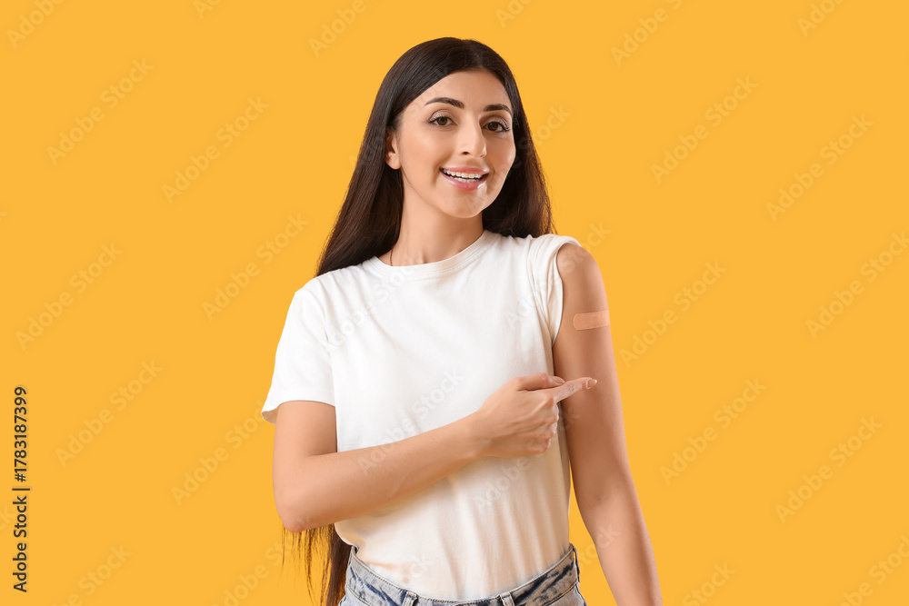 Obraz premium Young woman pointing at medical patch after vaccination on yellow background. Immunity concept
