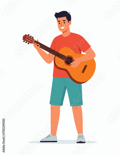 A young man stands and plays an acoustic guitar, smiling as he performs.