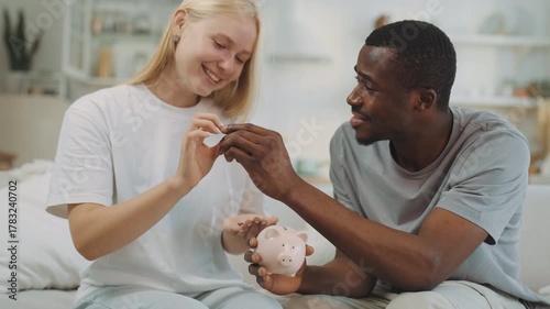 Save money and form family budget, woman and man putting coins into piggy bank. Portrait of happy interracial loving couple, financial literacy and savings for realize dreams, multiethnic couple