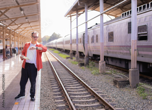 Quadro em tela Mature man holding a map and checking his watch while standing on a station plat