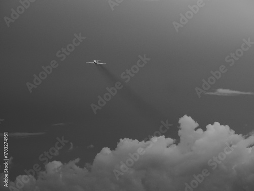black and white image of an airplane taking off in cloudy sky and producing a long track of dirty pollution plume