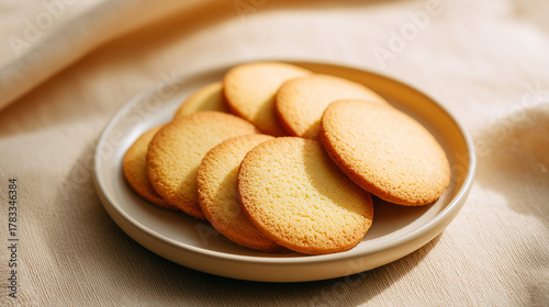 ベージュの布の上でベージュの皿に重ねられたシンプルな丸いバタークッキー